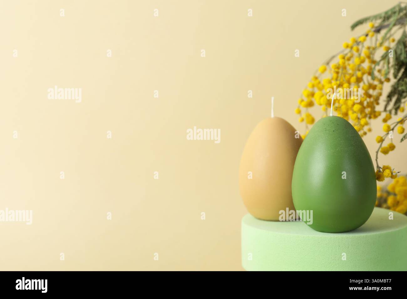 Beautiful egg shaped candles and mimosa flowers on beige background, closeup with space for text. Easter decor Stock Photo