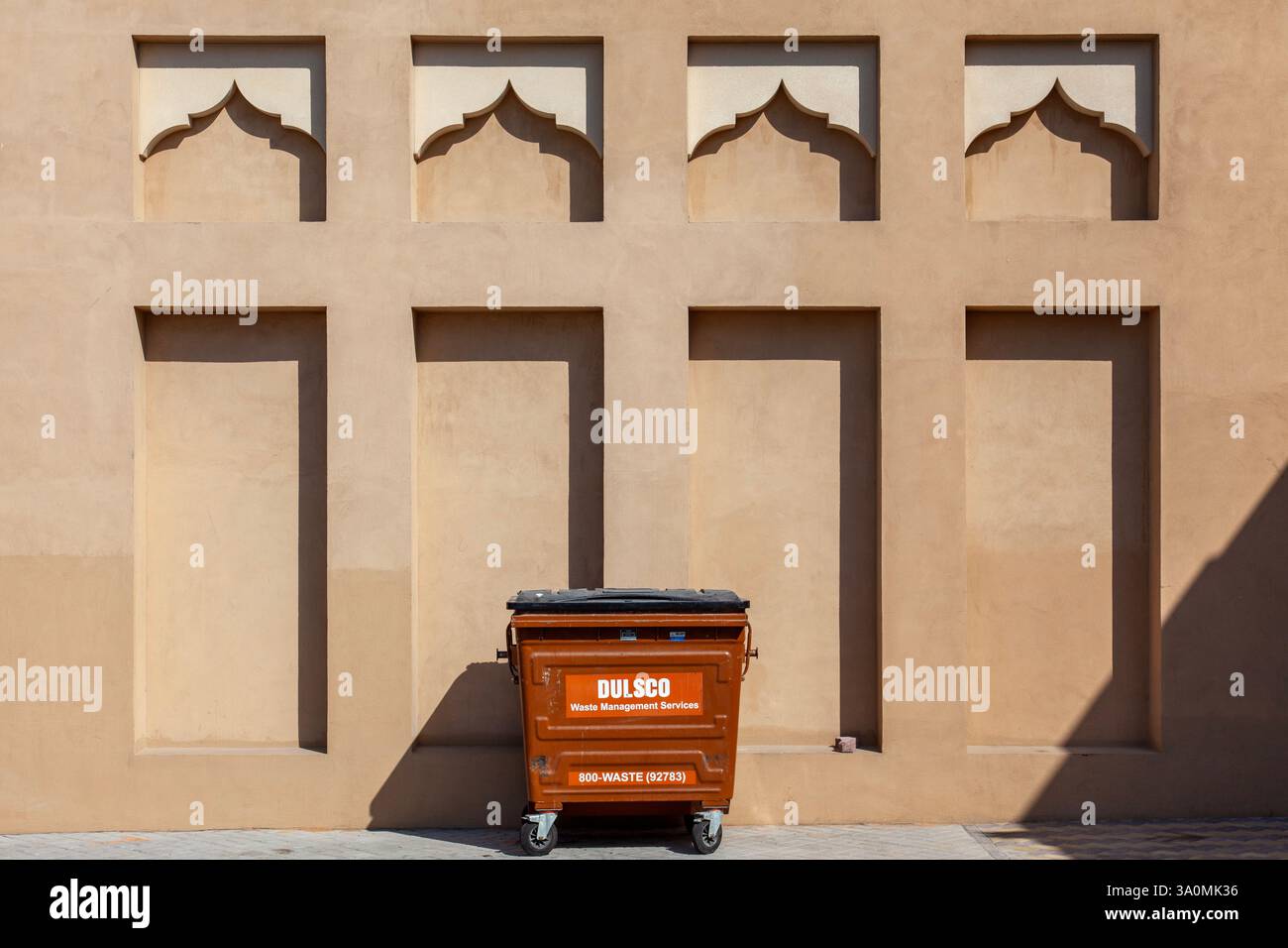 Traditional Arabic wall with ornate niches and a modern trash bin juxtaposition Stock Photo