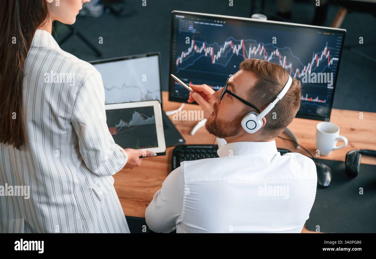 Two office workers are analyzing graphs that on the computer screen. Stock Photo