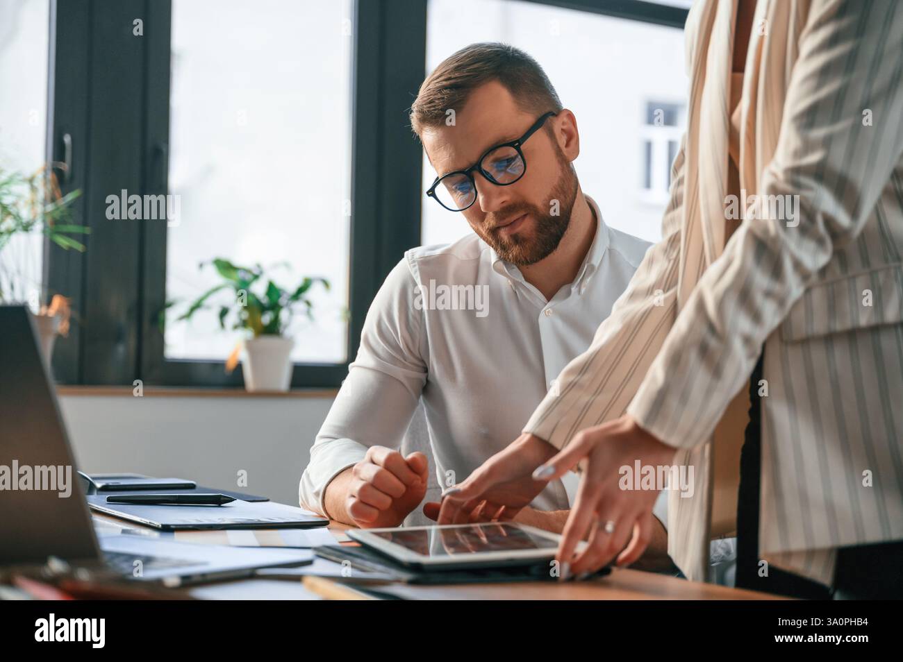 Woman is holding tablet, analysing information. Two employees are working together in the modern office. Stock Photo