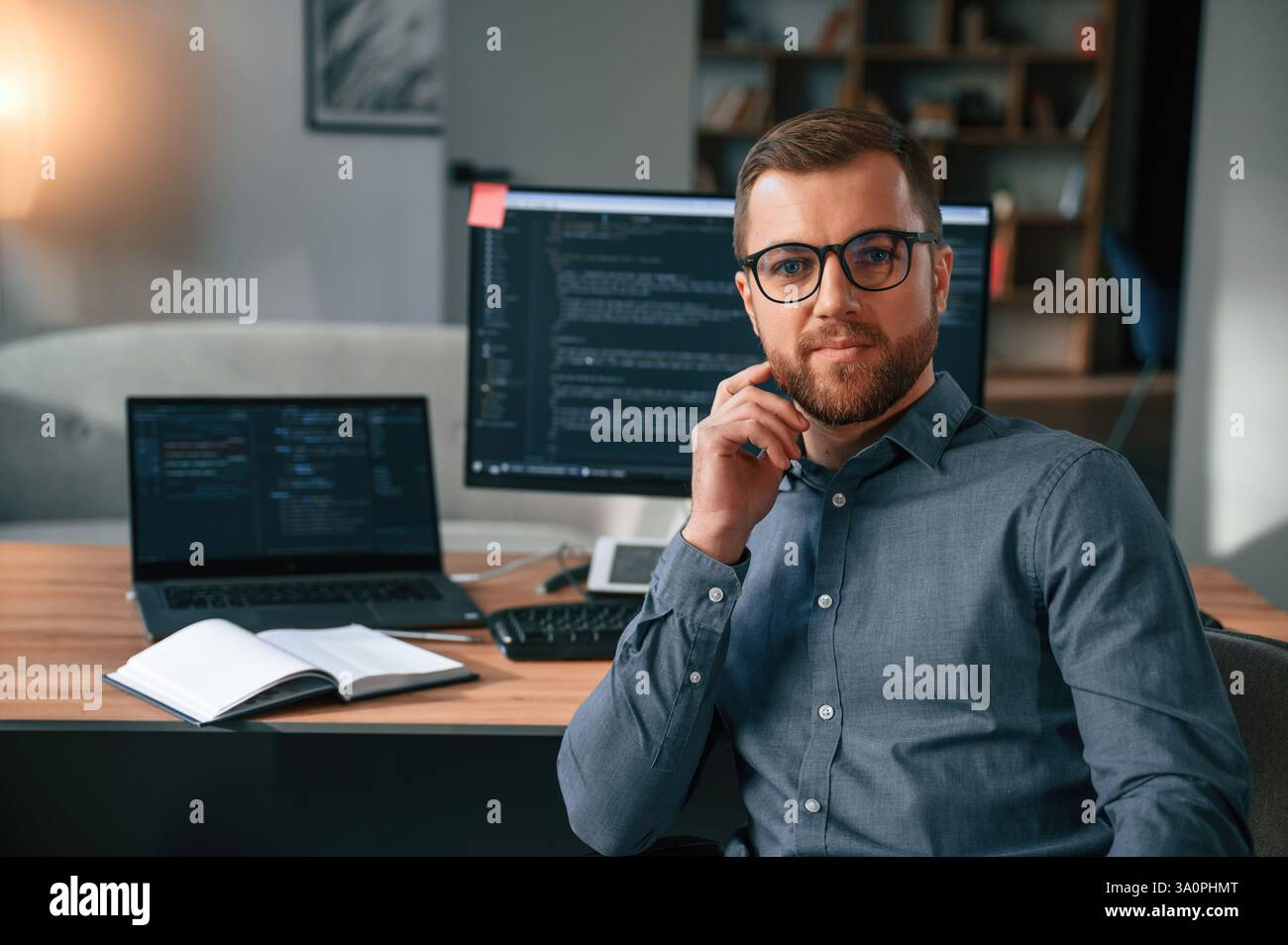 Software developer is sitting and posing. Man in formal clothes is working in the modern office. Using computer. Stock Photo