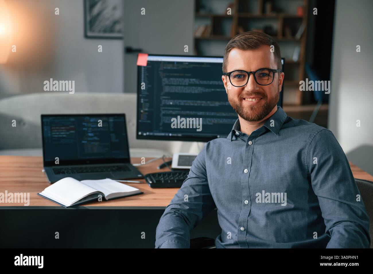 Software developer is sitting and posing. Man in formal clothes is working in the modern office. Using computer. Stock Photo