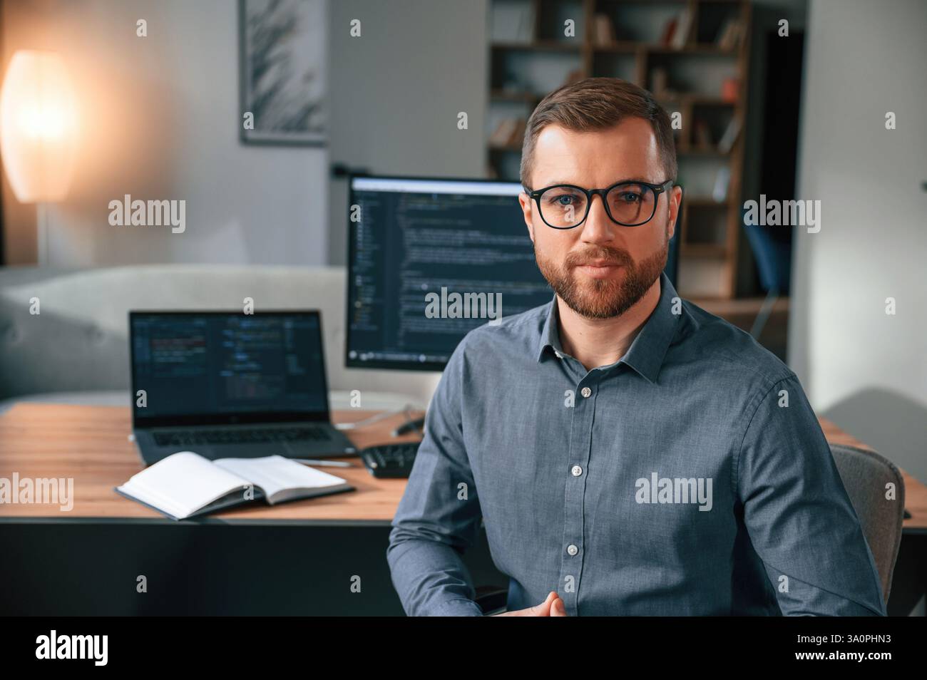 Software developer is sitting and posing. Man in formal clothes is working in the modern office. Using computer. Stock Photo
