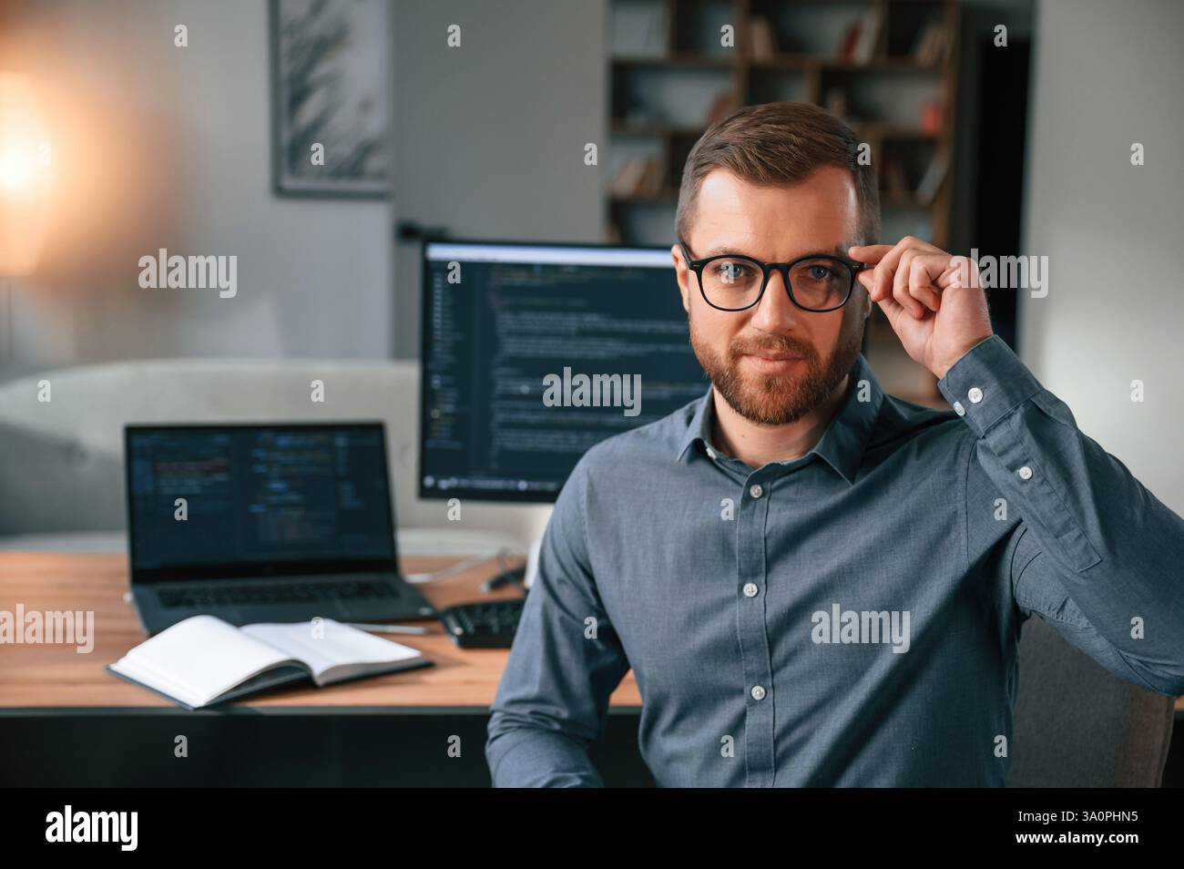 Software developer is sitting and posing. Man in formal clothes is working in the modern office. Using computer. Stock Photo