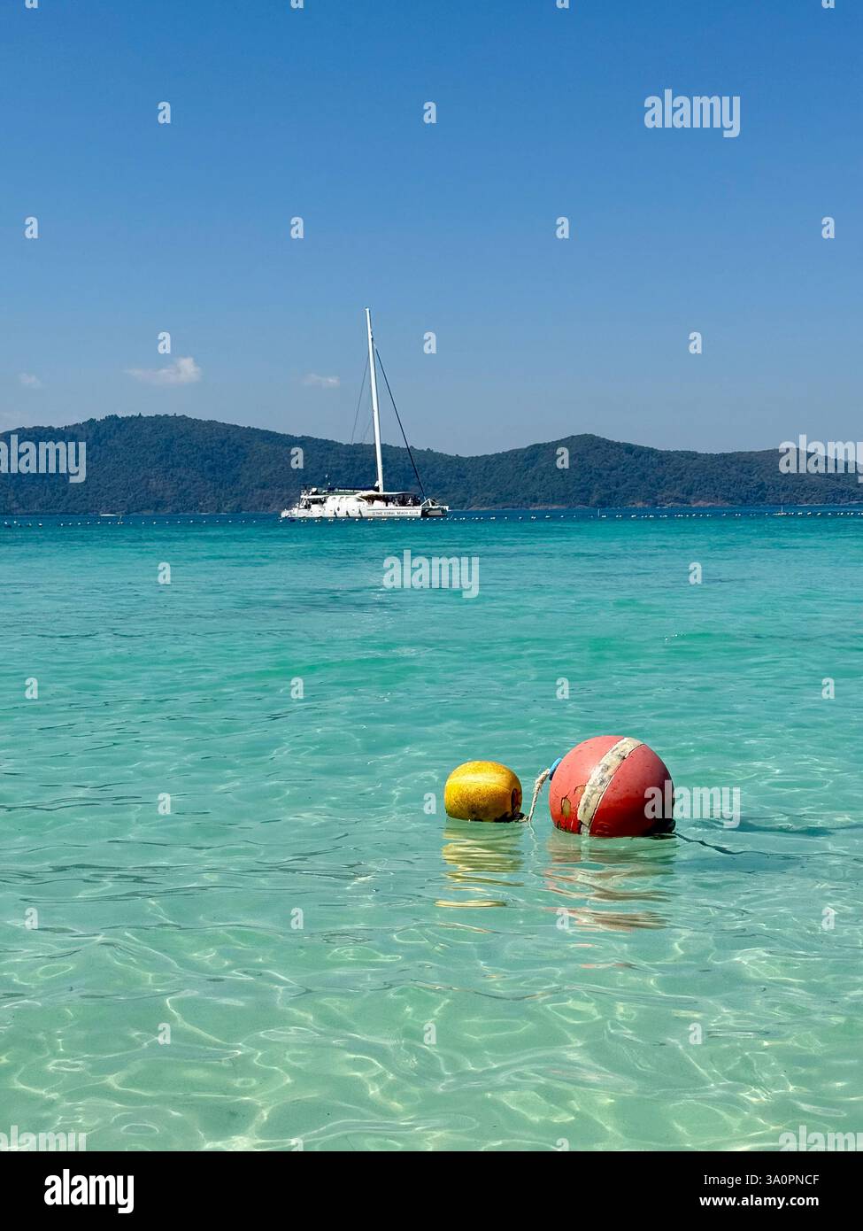 Floating Buoys in Crystal-Clear Waters Two colorful buoys, one red and one yellow, float gently on the stunning turquoise sea. In the background, a wh - Smartphone Captured Stock Image