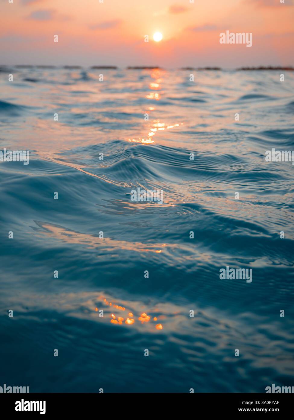 An abstract close up of warm turquoise sea reflecting the orange glints of a sunset in a tropical holiday location with the horizon and sky behind Stock Photo