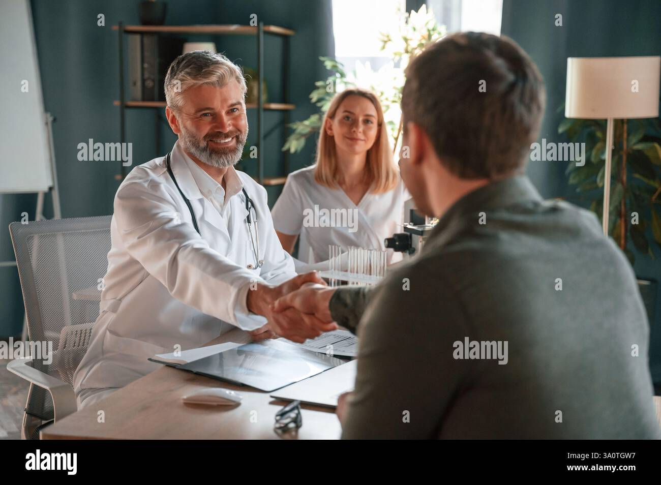 Greetings, making handshake. Two doctors consult a patient in a clinic. Stock Photo