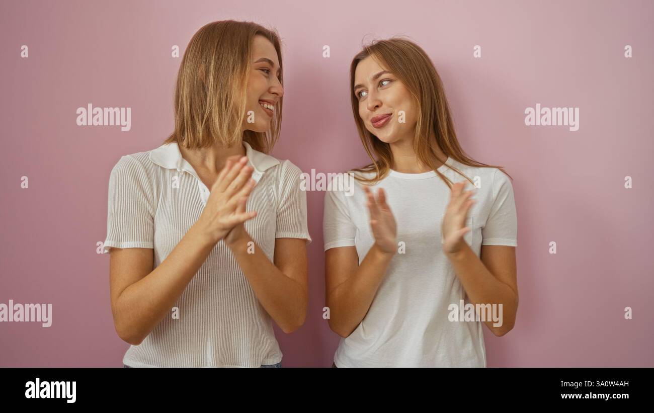 Two smiling blonde caucasian women clapping together against a pink ...