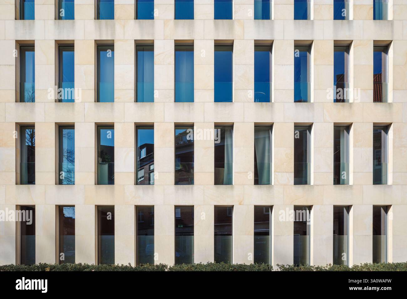 A contemporary building exterior featuring a beige stone facade with a repetitive pattern of narrow, rectangular windows. Stock Photo