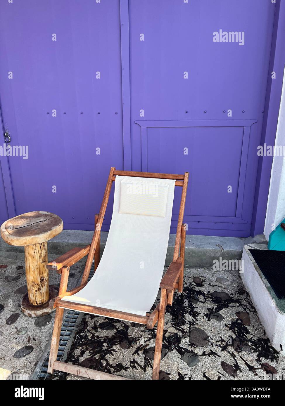 A wooden deck chair with a white sling sits by a bold purple wall - Smartphone Captured Stock Image