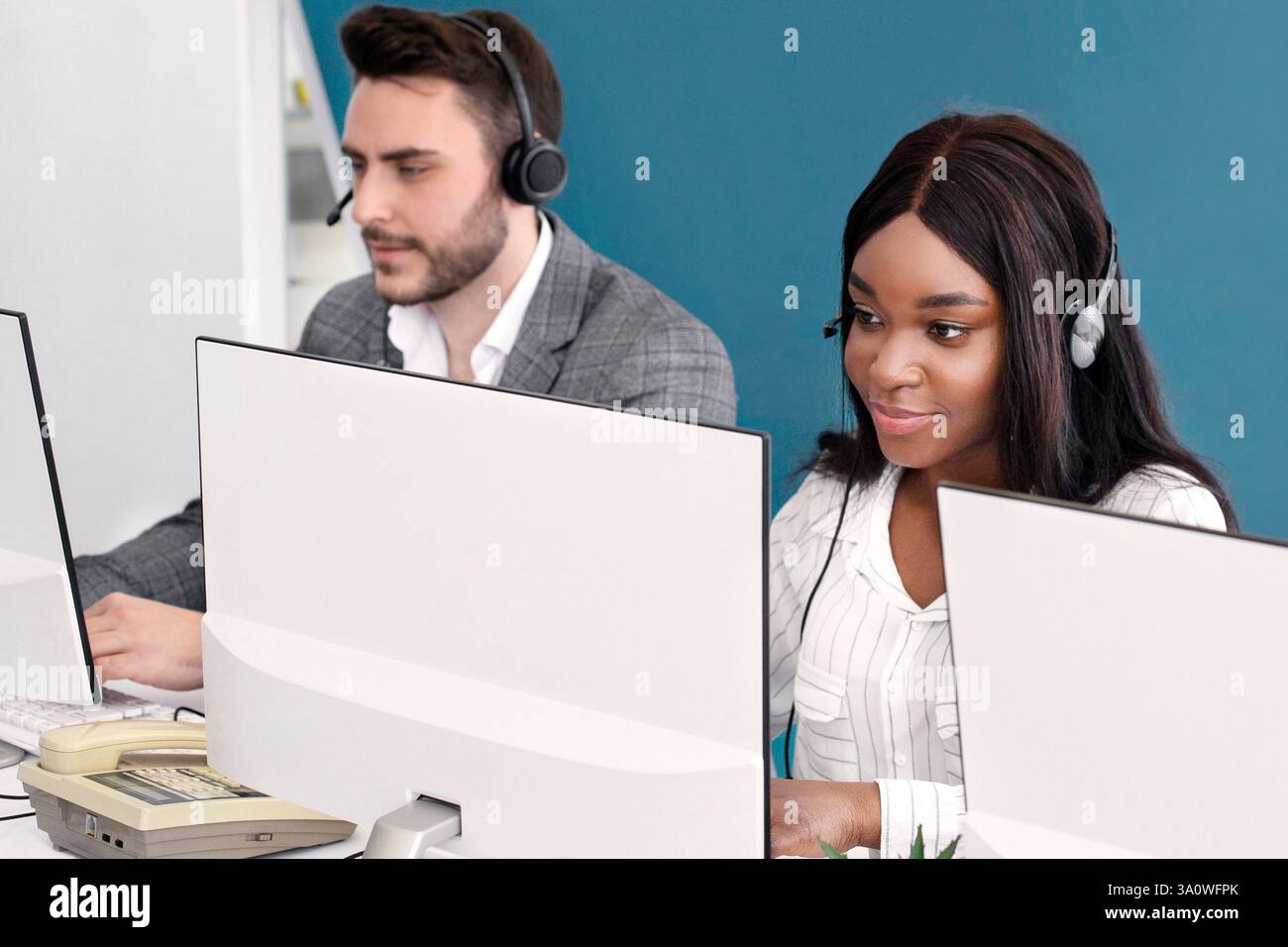 Focused call center operators with headsets working in front of computer monitors at open space office Stock Photo