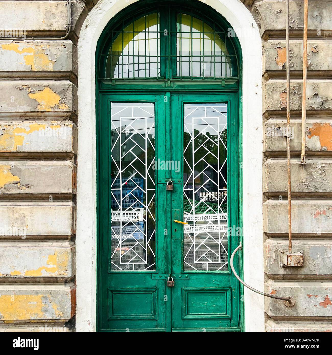 A weathered green door with iglass and metalwork, framed by the peeling facade of a historic building in Łódź - Smartphone Captured Stock Image