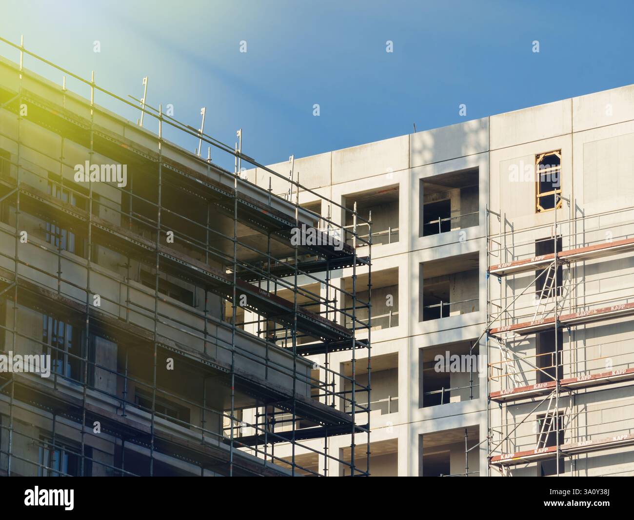 Construction scaffolding wraps around a large concrete building under development in soft evening light. Stock Photo