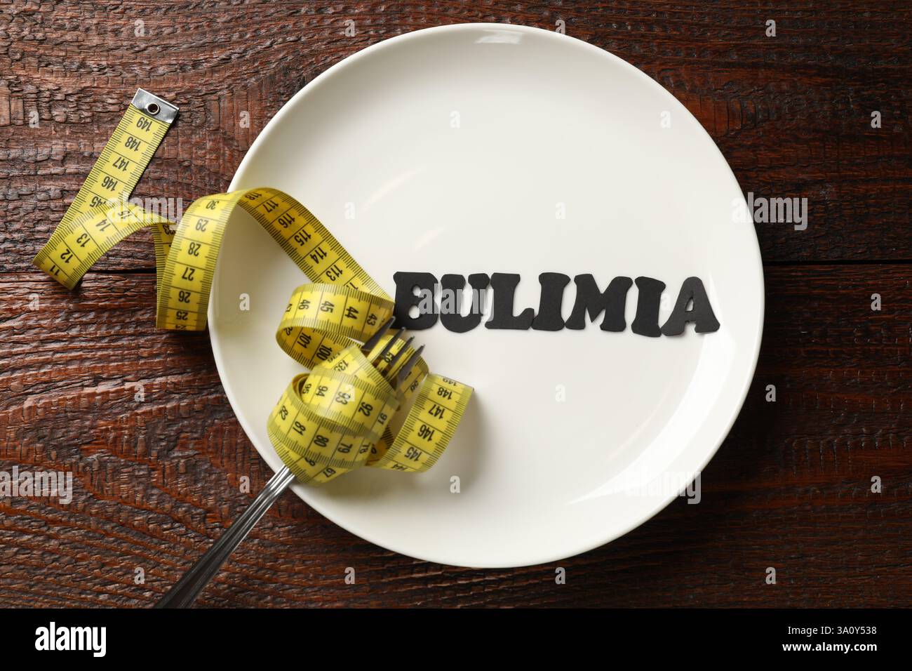 Plate with word Bulimia, fork and measuring tape on wooden table, top view Stock Photo