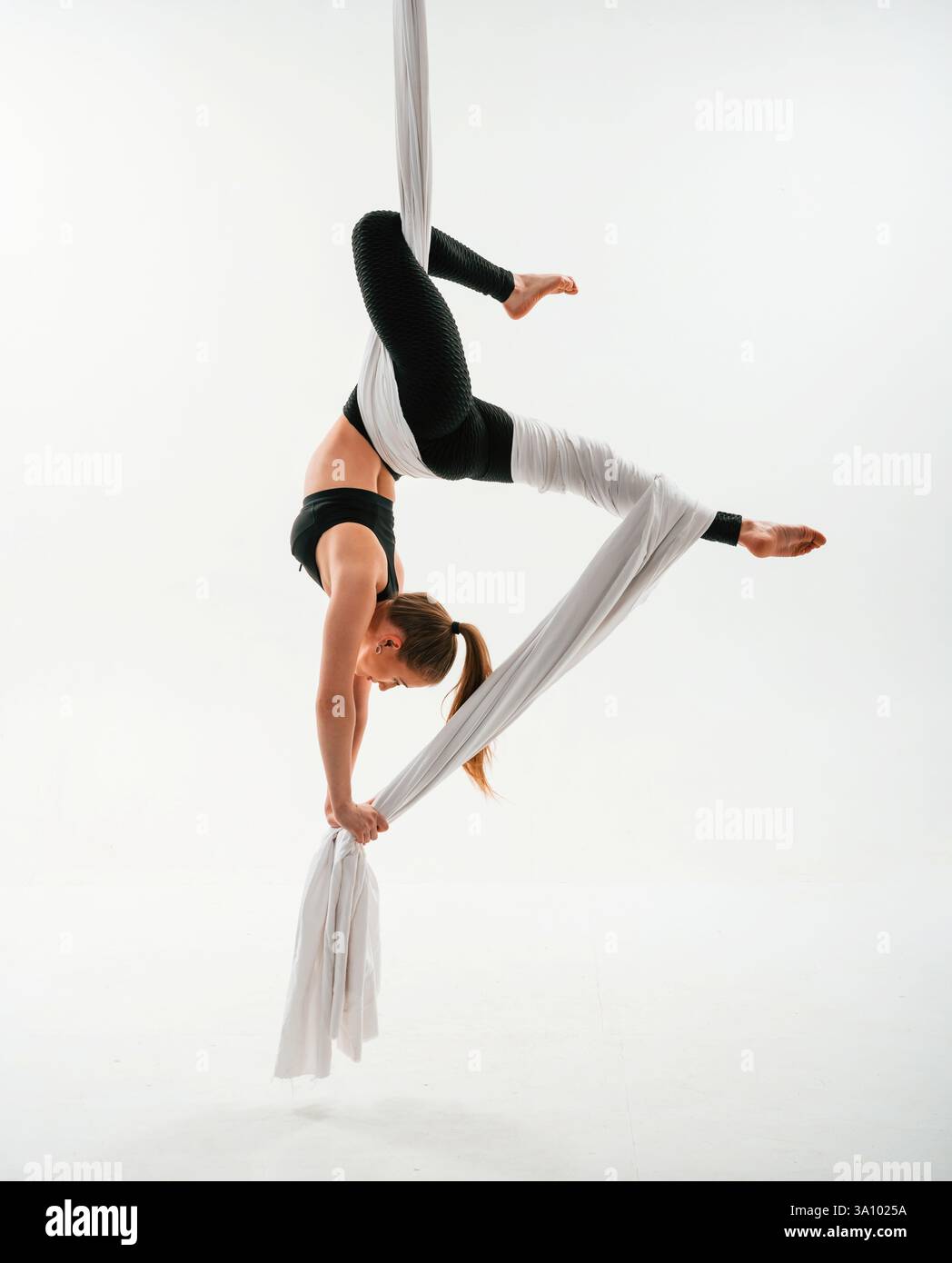 Hanging upside down. Young beautiful woman doing fly yoga against white ...