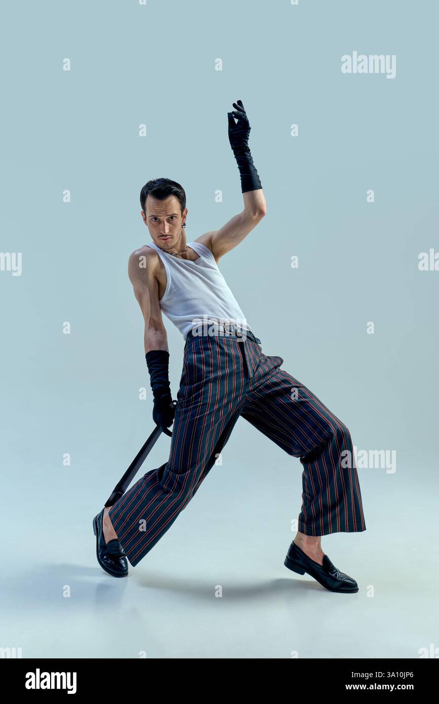 Dynamic performer striking powerful pose with intense gaze, gripping microphone in expressive dance motion against soft-toned studio background. Stock Photo