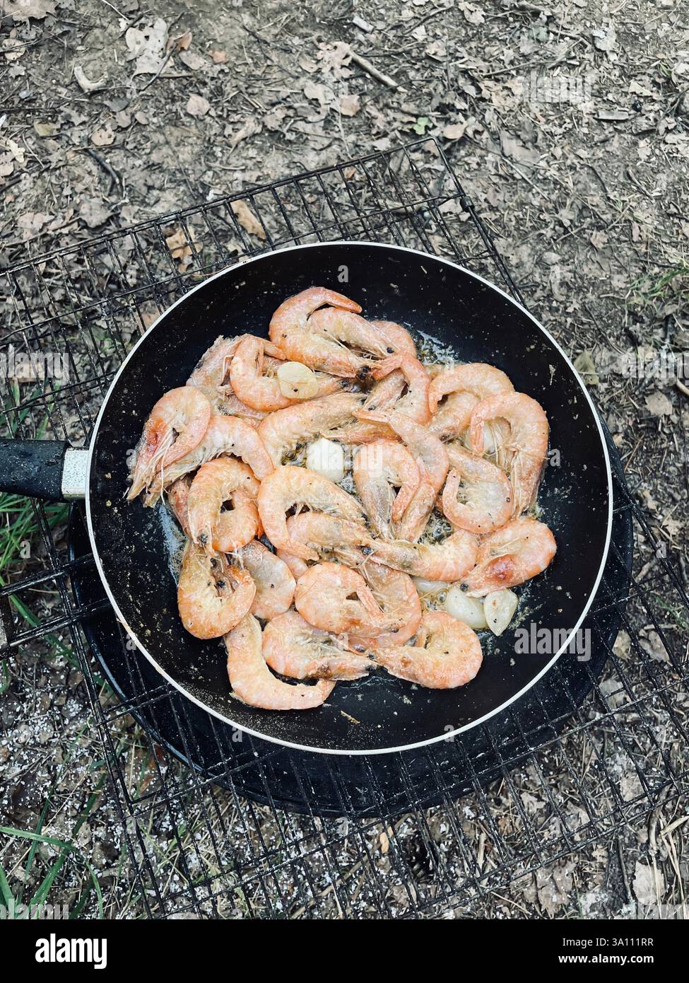 Freshly cooked shrimp sizzling in a pan outdoors, capturing the essence of a simple, delicious meal with a touch of nature's backdrop. - Smartphone Captured Stock Image