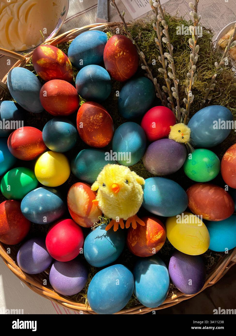 A vibrant display of colorful Easter eggs, nestled in a wicker basket with a charming plush chick for a festive celebration. - Smartphone Captured Stock Image