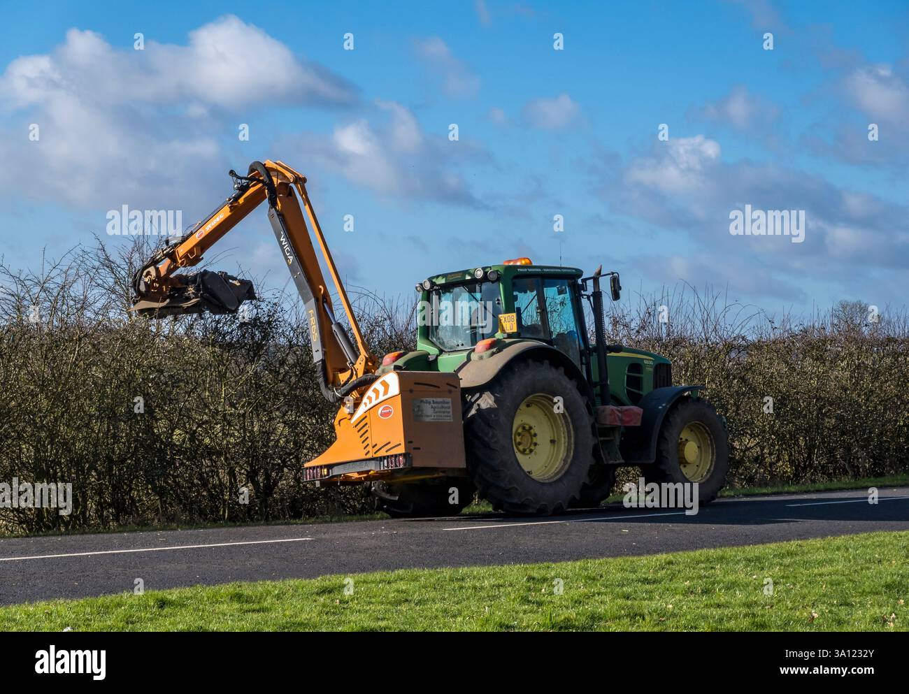Trimming hedge tops with motorised trimmer on back of John Deere  tractor Stock Photo