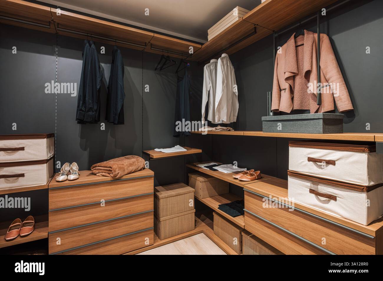 Modern and organized walk in closet featuring wooden furniture, gray walls, and neatly arranged clothes and accessories Stock Photo