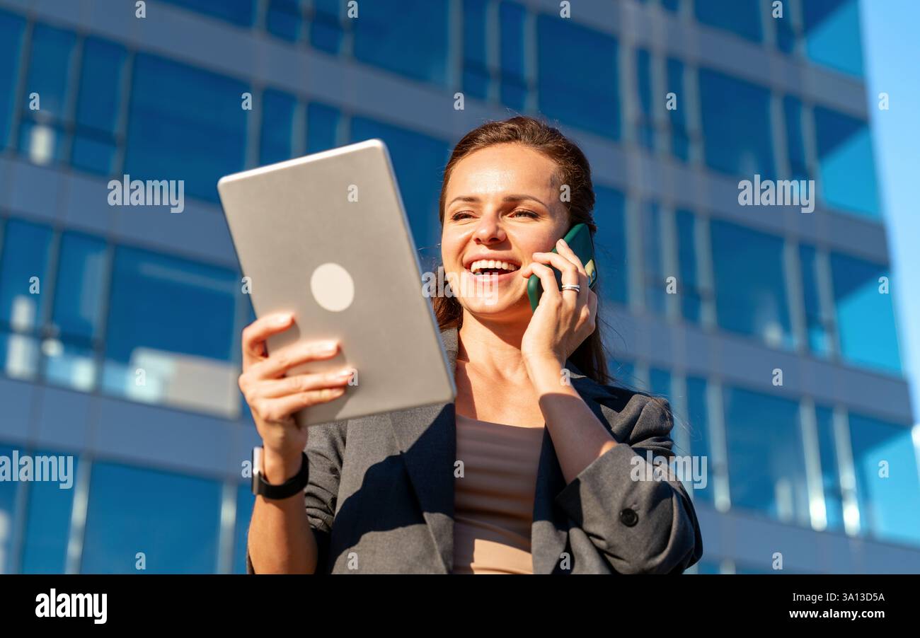 Businesswoman talking on mobile phone while looking at digital tablet Stock Photo