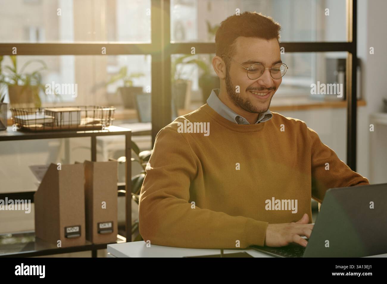 Smiling Man Using Computer in Office Lit By Sunlight Stock Photo