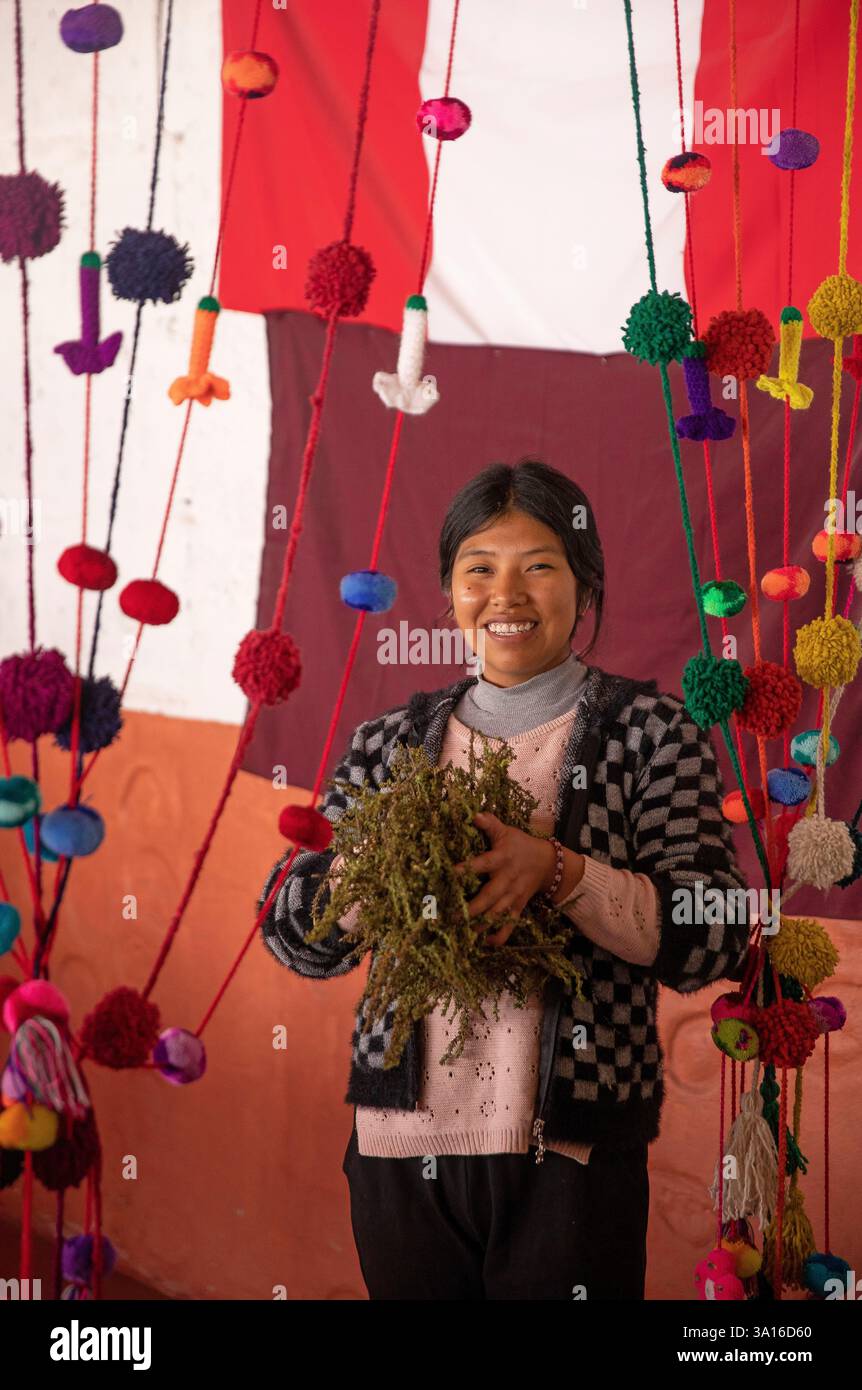 Peru, Andes Cordillera, national reserve of Salinas y Aguada Blanca, young Amerindian woman holding aromatic herbs in her hands in a setting of colourful tasselled garlands Stock Photo