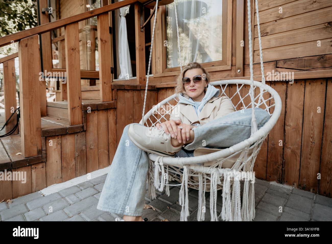 Woman Relaxing in a Hanging Chair on a Wooden Patio Stock Photo - Alamy