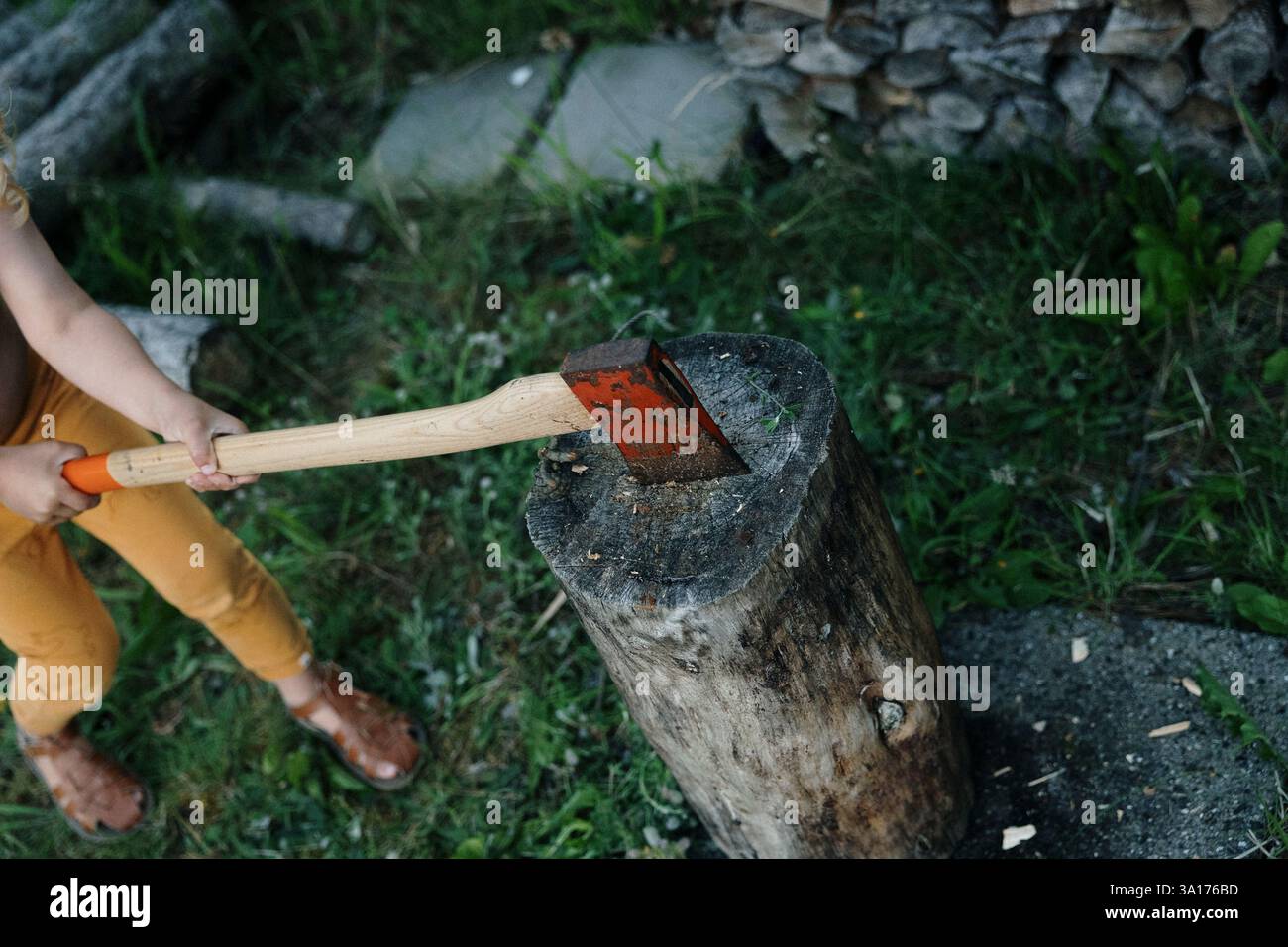 Child holding an axe embedded in a chopping block outdoors Stock Photo