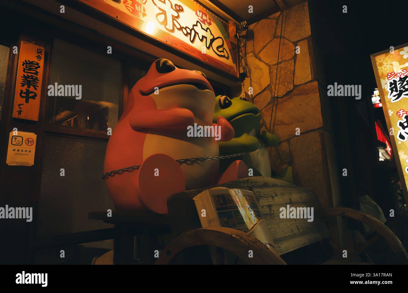 Two colorful cartoony frog statues, chained outside a small restaurant in Shinjuku Stock Photo