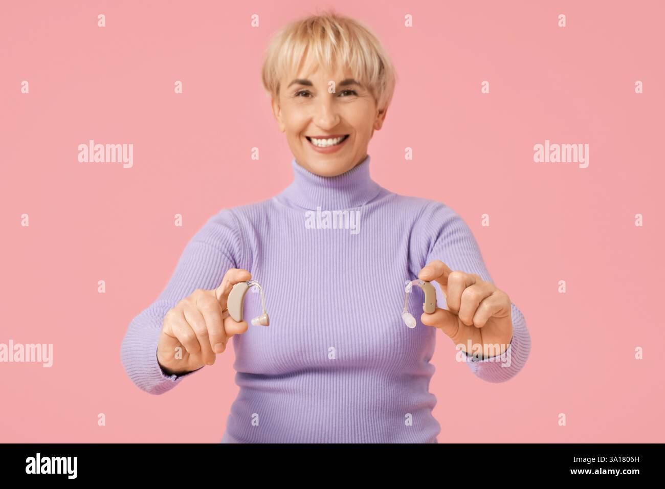 Mature woman with hearing aids on  pink background Stock Photo