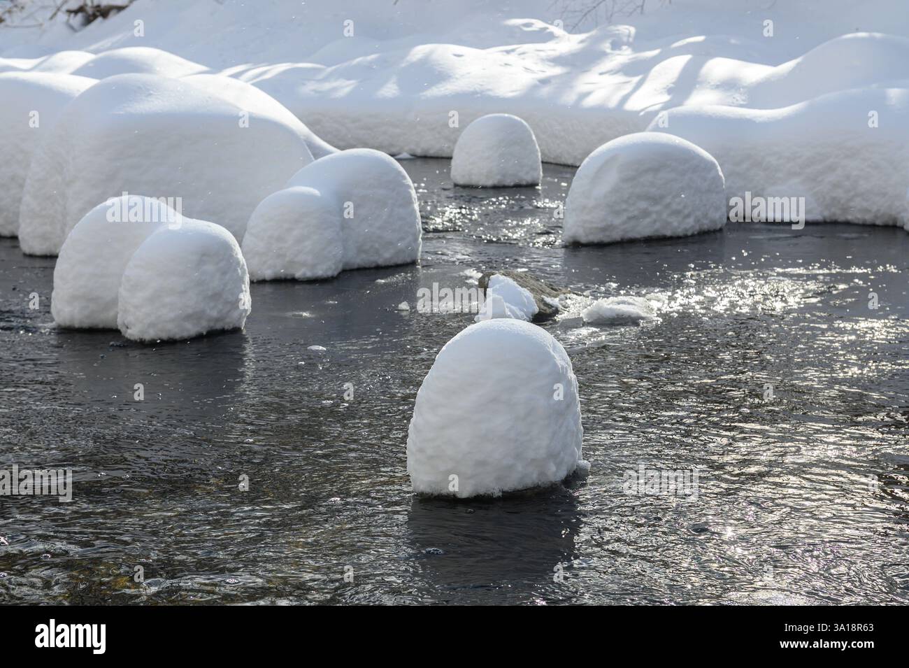 Large rocks covered in thick snow sit in a flowing creek, creating a ...