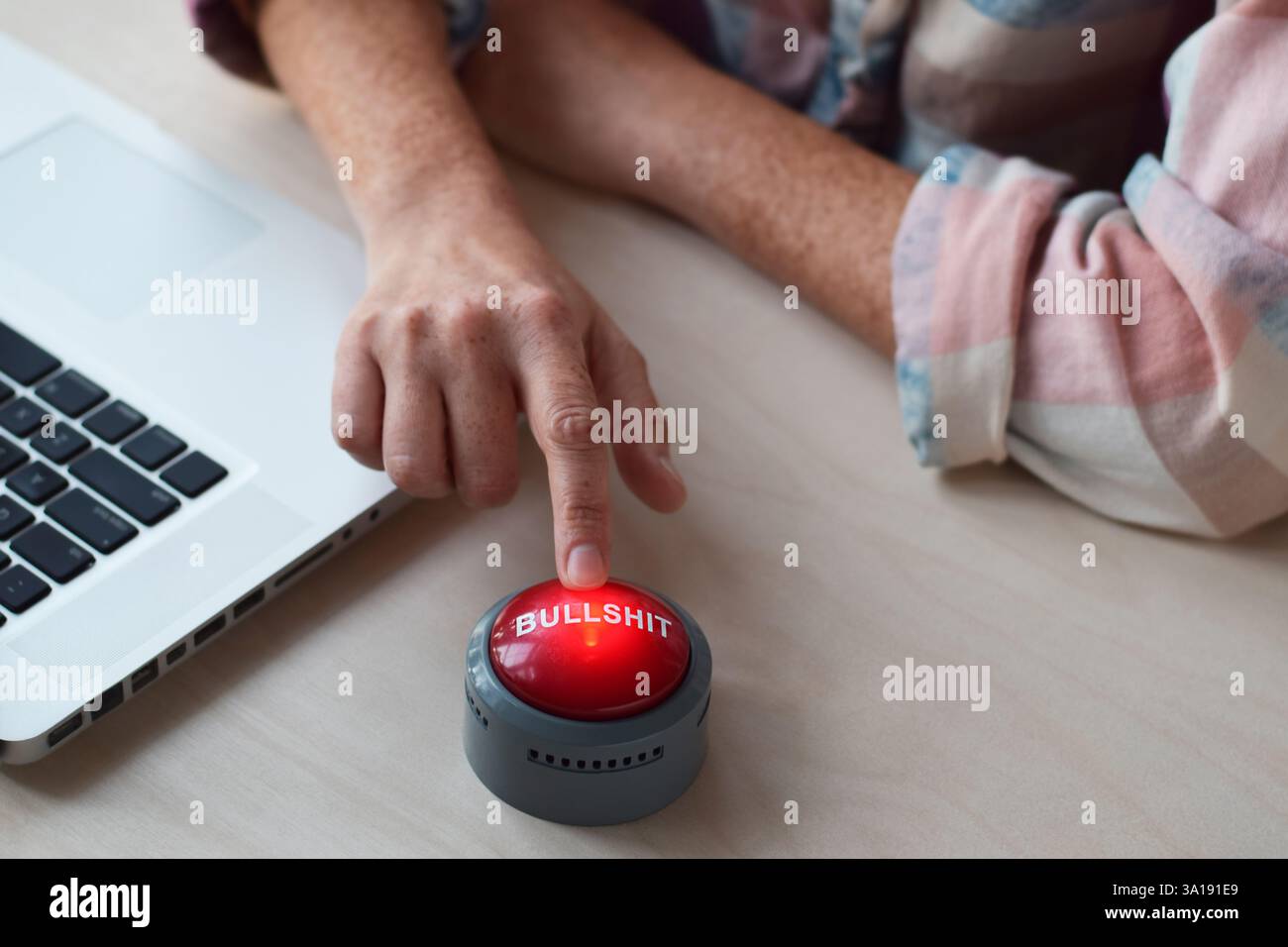 Closeup on woman's hand finger pressing red Bullshit button sitting at a desk Stock Photo