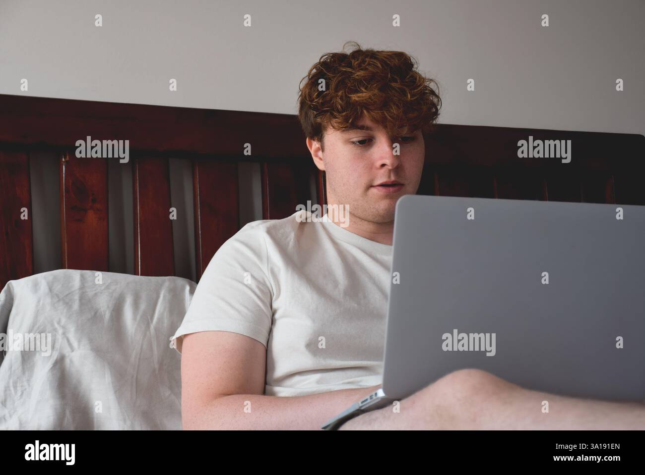 Young man sitting on bed using laptop computer Stock Photo