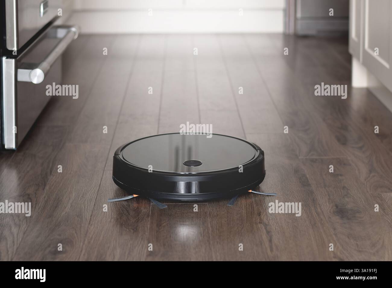 Robot vacuum cleaner cleaning kitchen hardwood floor Stock Photo