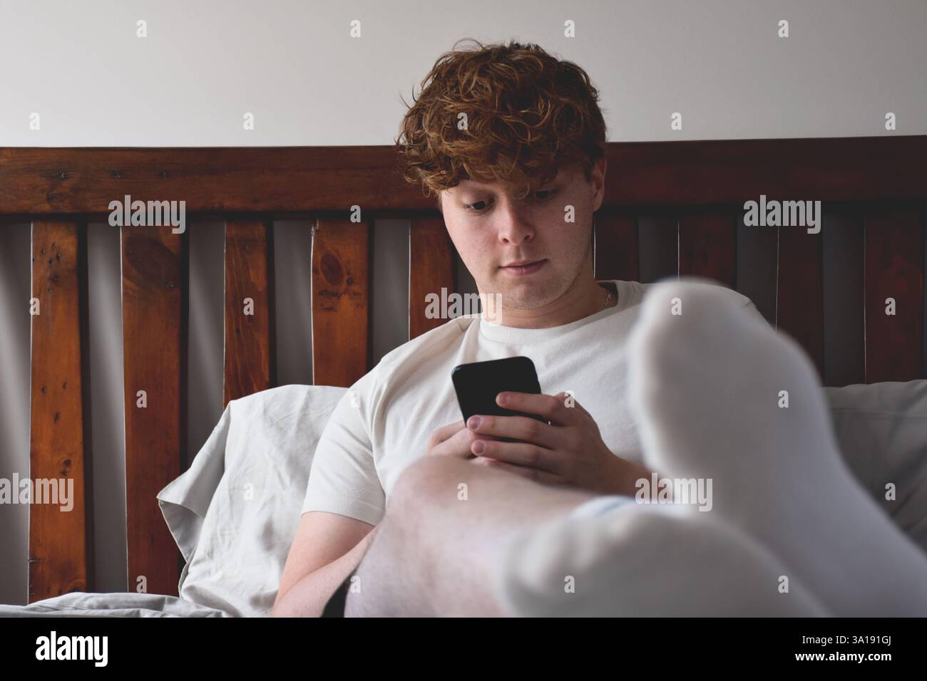 Young man sitting on bed using mobile phone Stock Photo