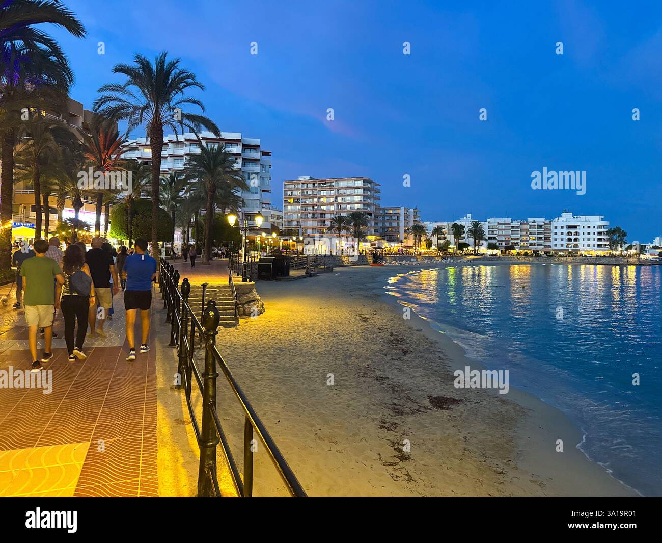 Walking into Santa Eularia on the boardwalk next to the beach and the Mediterranean Sea at dusk as the marina lights come on and the restaurants open Stock Photo