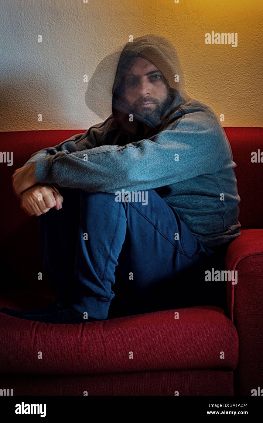 Depressed man, with hood on his head, sitting alone on a sofa. Double ...