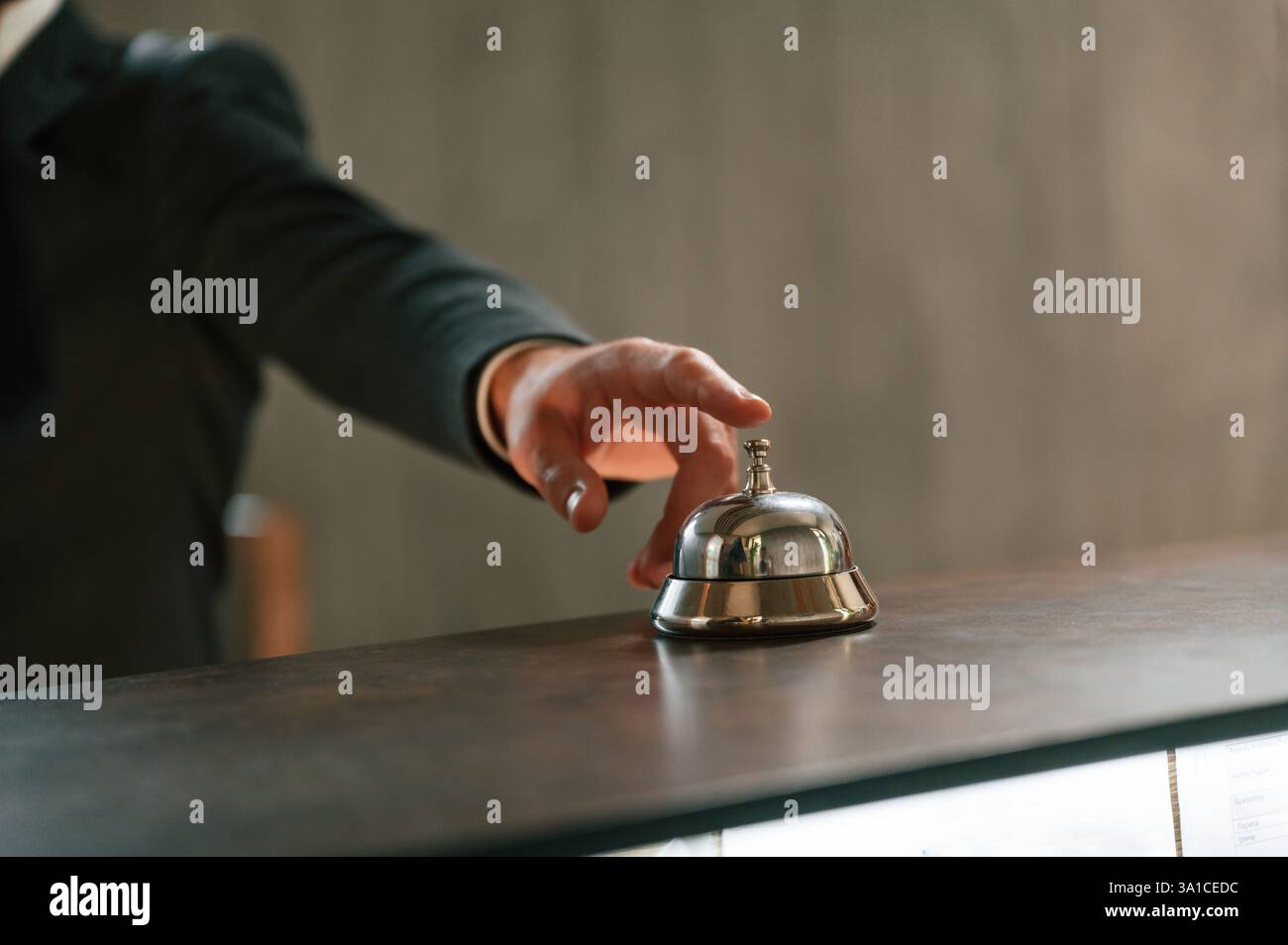 Close up view, using hotel desk bell. A man in a black jacket at the hotel reception. Stock Photo