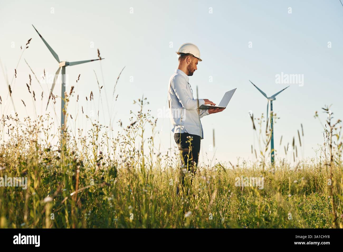 Working by using laptop. Service engineer is on the field with windmills. Stock Photo