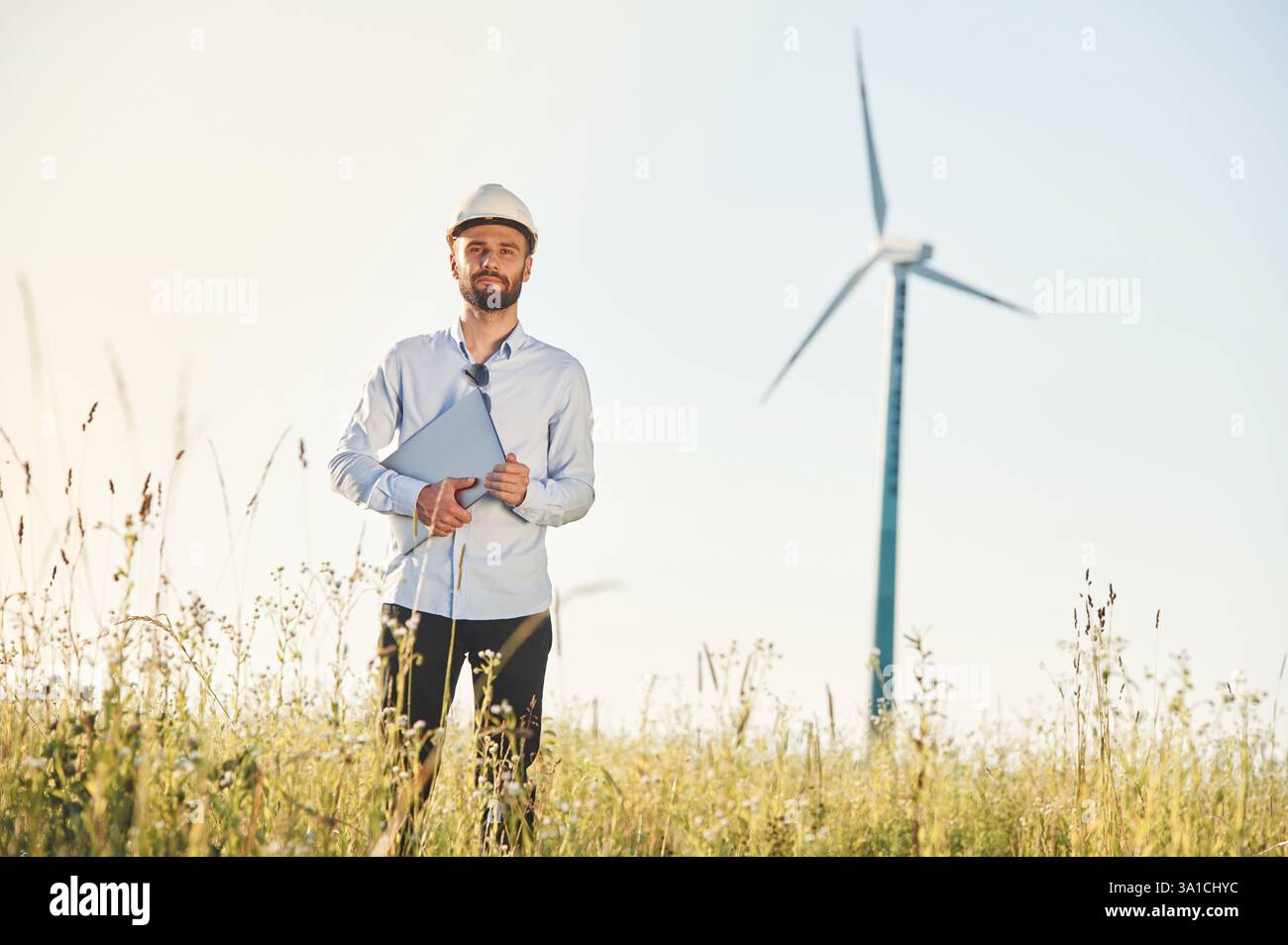 Working by using laptop. Service engineer is on the field with windmills. Stock Photo
