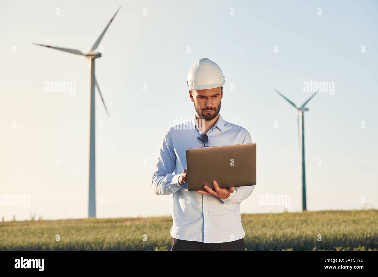 Working by using laptop. Service engineer is on the field with windmills. Stock Photo