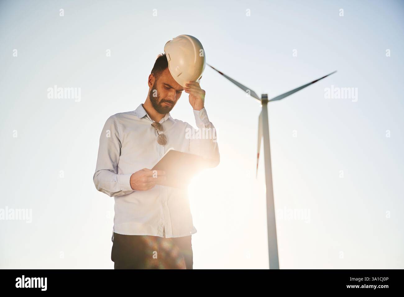 Standing against sunlight. Notepad in hands. Service engineer is on the field with windmills. Stock Photo