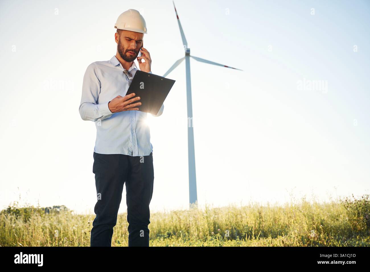 Standing against sunlight. Notepad in hands. Service engineer is on the field with windmills. Stock Photo