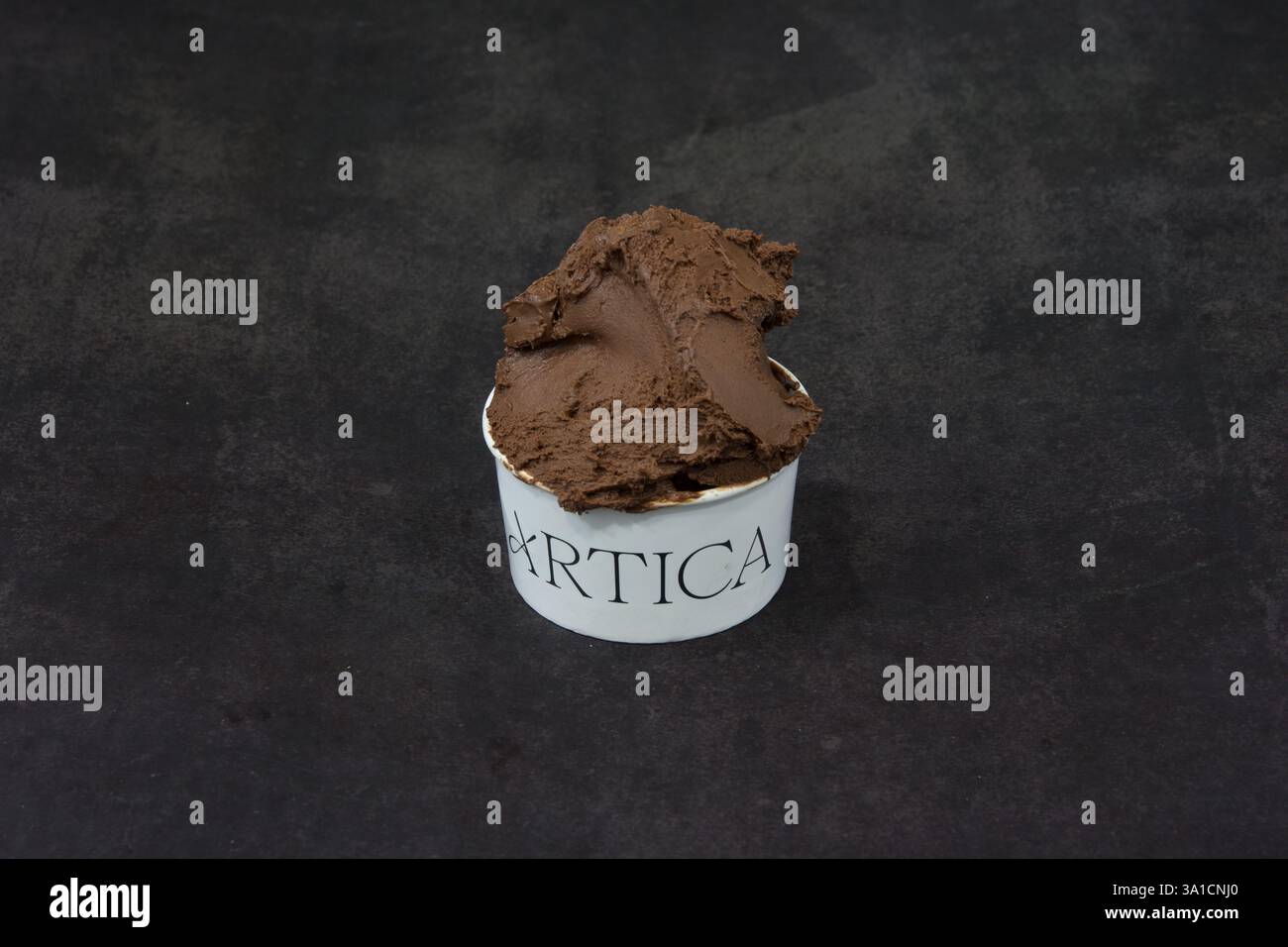 A scoop of chocolate ice cream in a white bowl with the word Arctica written on it. The bowl is sitting on a dark surface Stock Photo