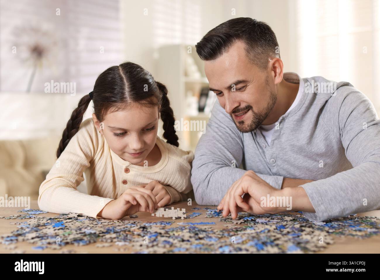 Happy father and his daughter solving puzzle together at wooden table
