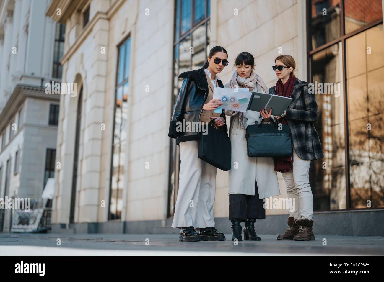 Three businesswomen collaborating outdoors while reviewing documents and discussing ideas Stock Photo