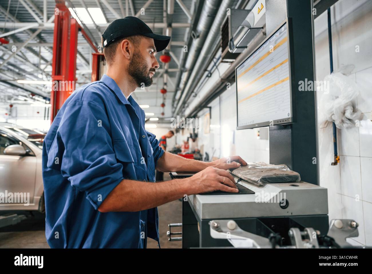 Side view, using computer. Auto mechanic working in garage. Repair service. Stock Photo
