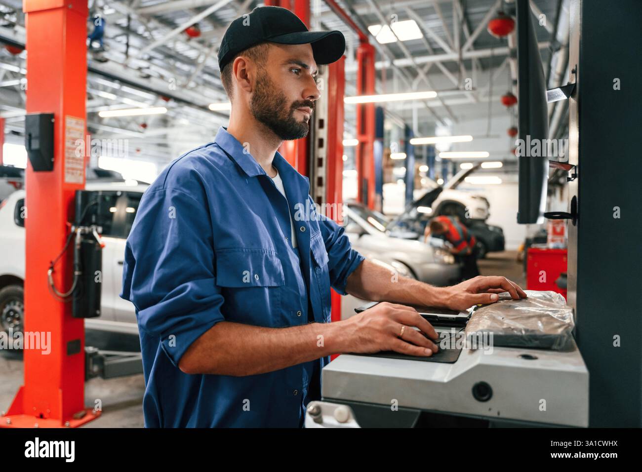 Side view, using computer. Auto mechanic working in garage. Repair service. Stock Photo