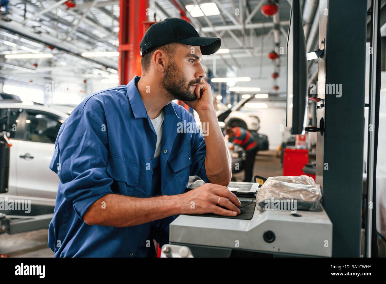 Side view, using computer. Auto mechanic working in garage. Repair service. Stock Photo